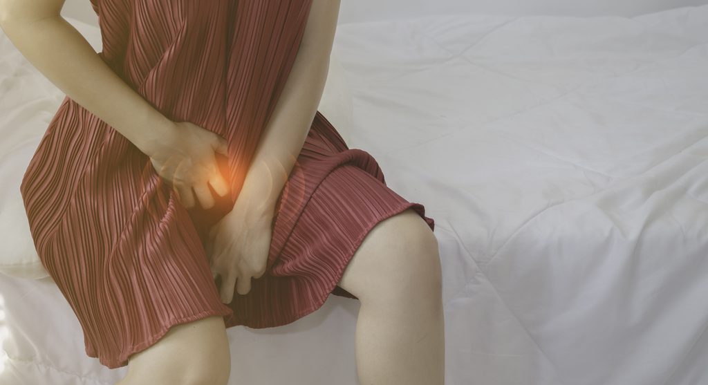 침대에 앉아 회음부 쪽을 손으로 감싸고 있는 여성